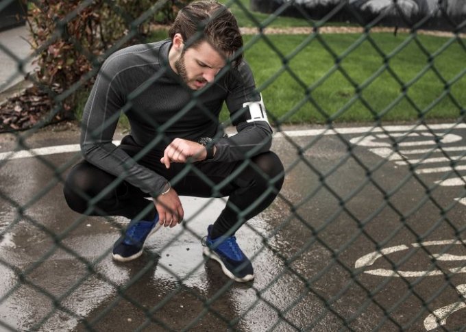 Mężczyzna biegający w deszczu ustawia funkcje sportowe w swoim wodoszczelnym smartwatchu