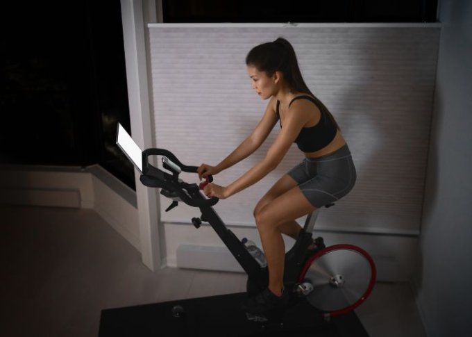 Kobieta na trenuje na interaktywnym trenażerze rowerowym w domu